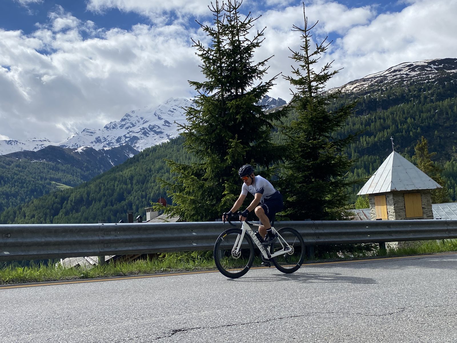 A rider climbing a quiet alpine road below snow-covered peaks